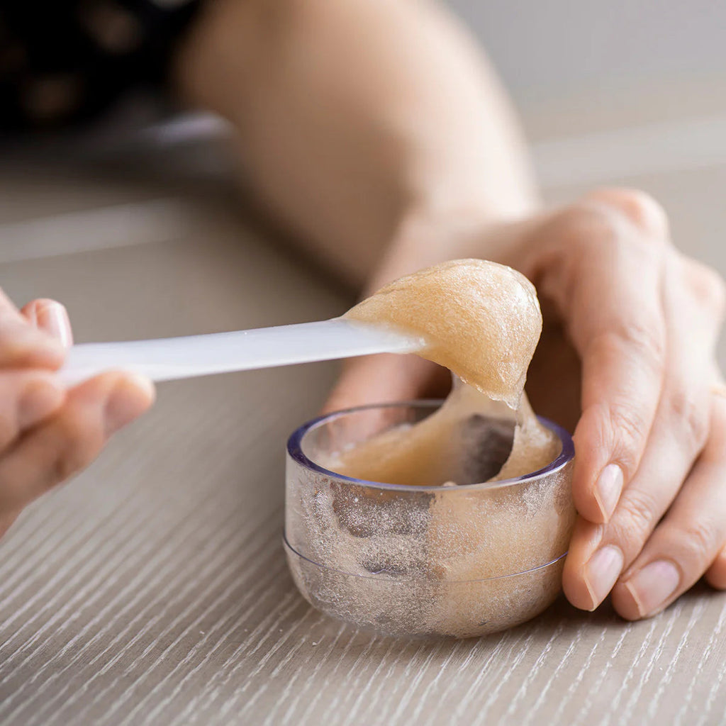 Person preparing a skincare product using a small container.